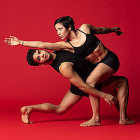A dancer stands strong and upright while holding up another dancer at his waist.