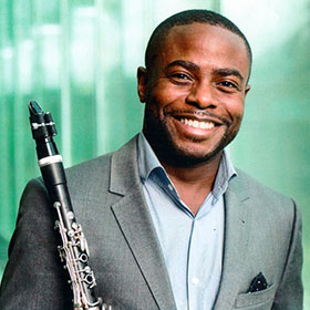 Anthony McGill holds his clarinet to his shoulder and smiles.