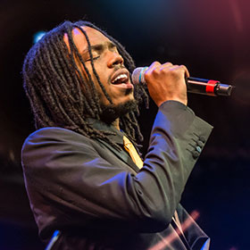 A Black choir singer holds a microphone up to his mouth as he sings expressively with his eyes shut.