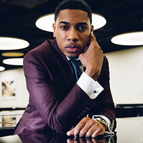 Christian Sands leans against the piano top.