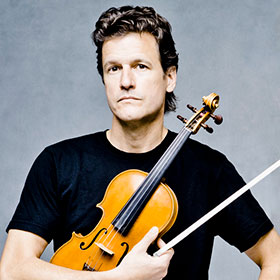 Geoff Nuttall stands holding his violin against his chest.